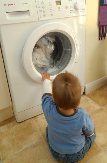 Little boy looking at laundry spinning in front loading machine
